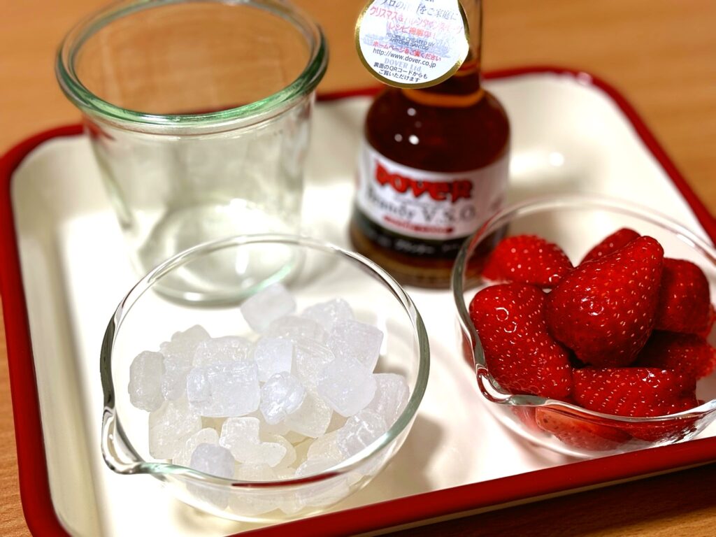 Strawberries, rock sugar, brandy, and a glass jar arranged on a tray.