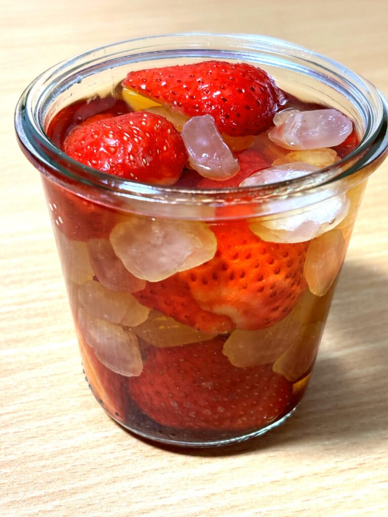 Strawberries and rock sugar soaking in brandy inside a glass jar.