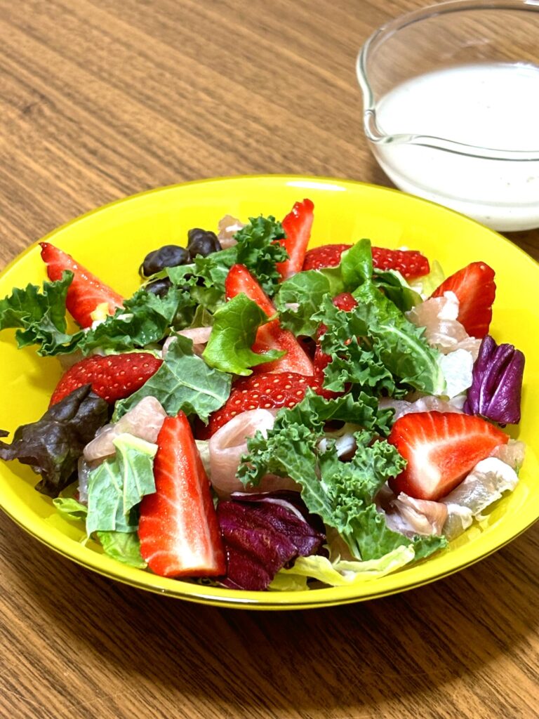 A colorful salad of strawberries, prosciutto, and mixed greens, served with French dressing on the side.