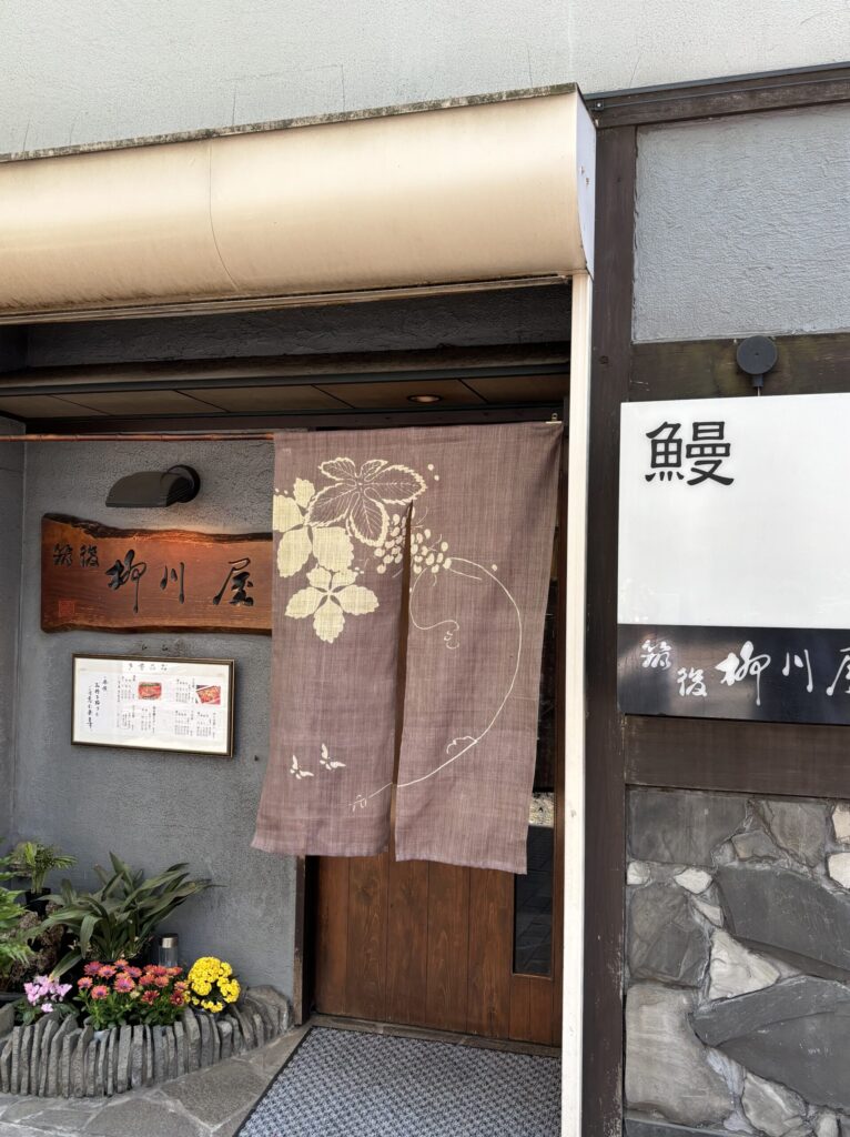 Exterior of a traditional eel restaurant with a wooden sign and floral-patterned noren curtain