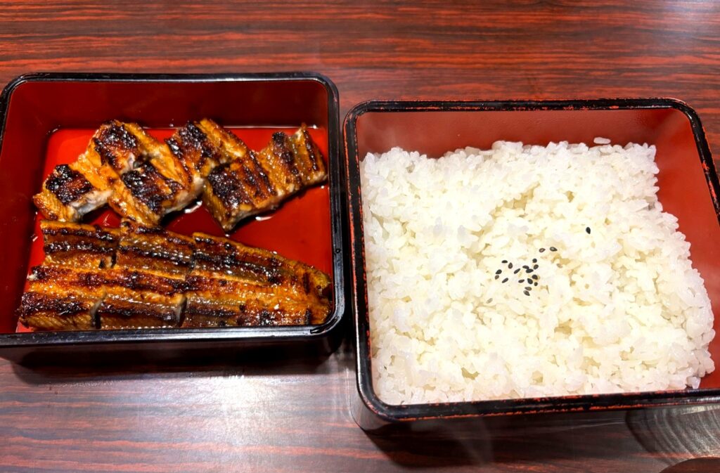 Grilled eel served in a lacquered box with steamed white rice topped with black sesame seeds