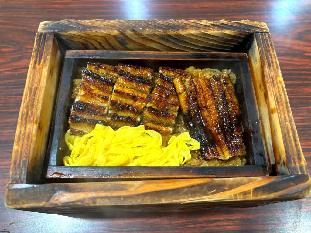 Grilled eel and shredded omelet served over steamed rice in a wooden seiro