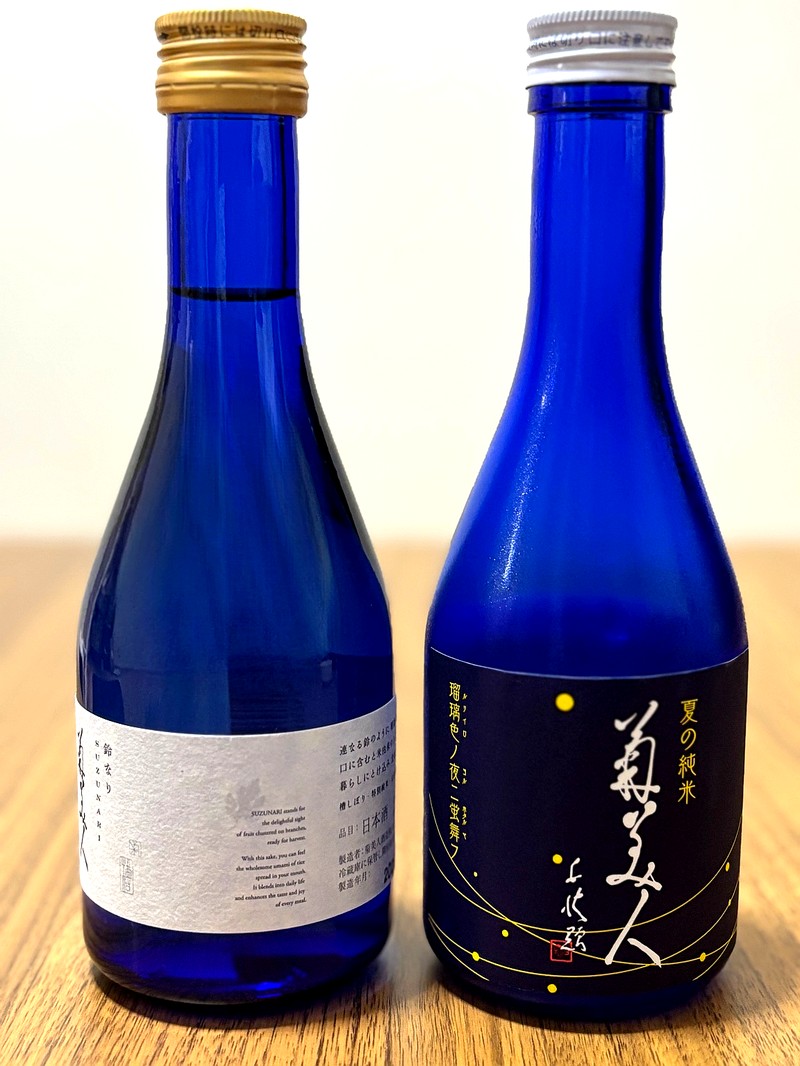 Two bottles of Kikubijin sake in deep blue glass: “Summer Junmai - Fireflies Dancing in the Lapis Night” and “Suzunari”.