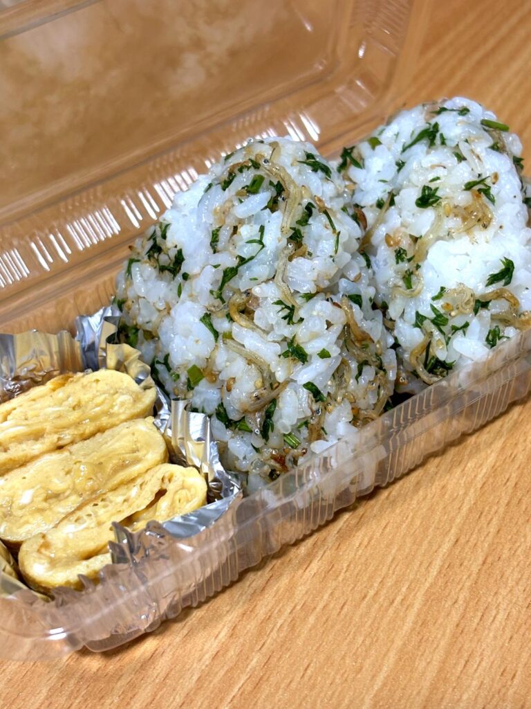 Rice balls mixed with carrot leaf furikake and plain salted egg rolls in a bento box