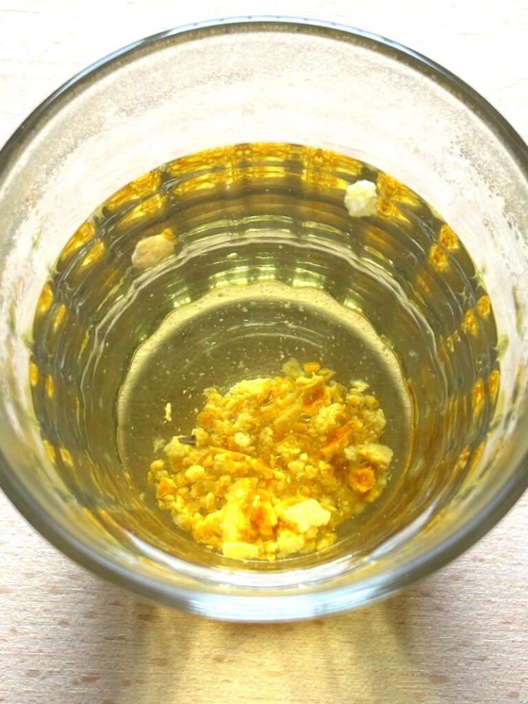 A glass of warm water infused with dried mandarin peel (chenpi), with finely crushed orange peel settled at the bottom and a faint yellow hue in the water.