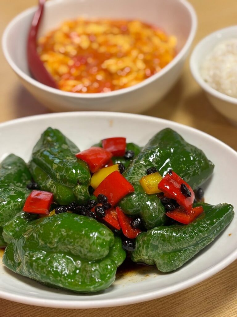 Stir-fried green peppers with fermented black beans, with tomato and egg stir-fry and rice in the background