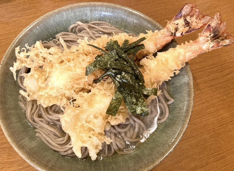 A bowl of tempura soba with two large crispy shrimp tempura on top.