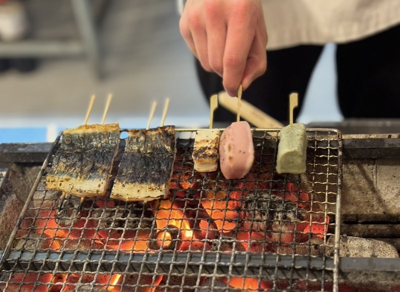 Grilled eel skewers and colorful "Namafu Dengaku" on a charcoal grill. The rich aroma of the charcoal enhances the mouthwatering appeal.