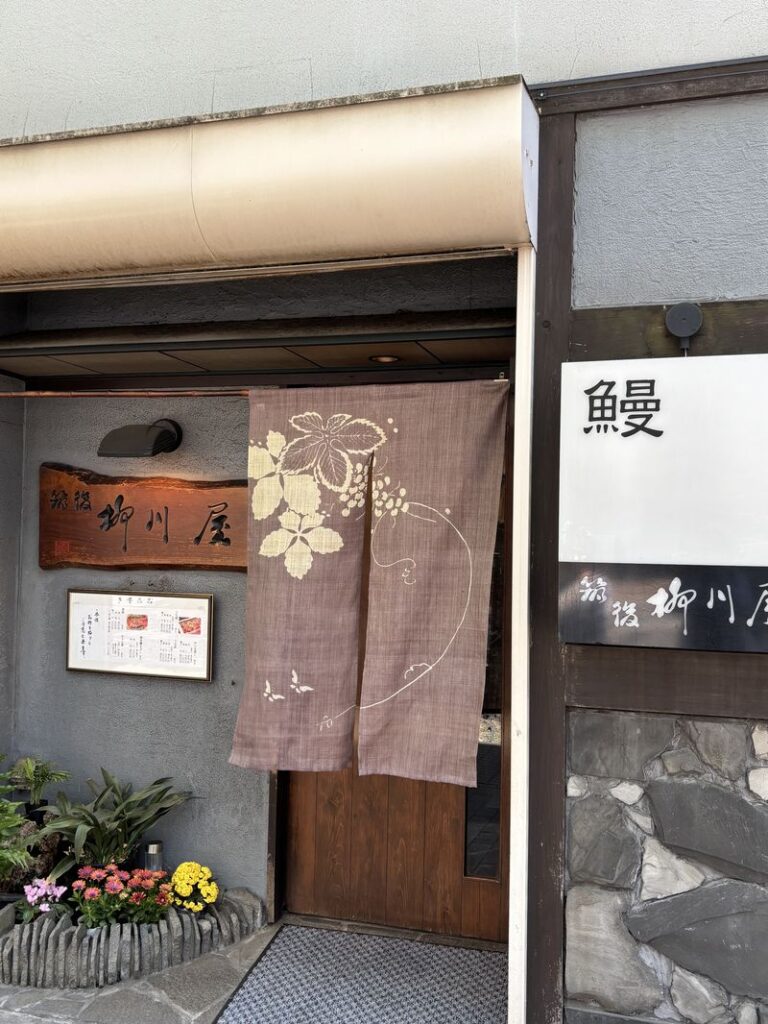 Exterior of a traditional eel restaurant with a wooden sign and floral-patterned noren curtain