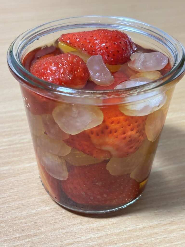 Strawberries and rock sugar soaking in brandy inside a glass jar.