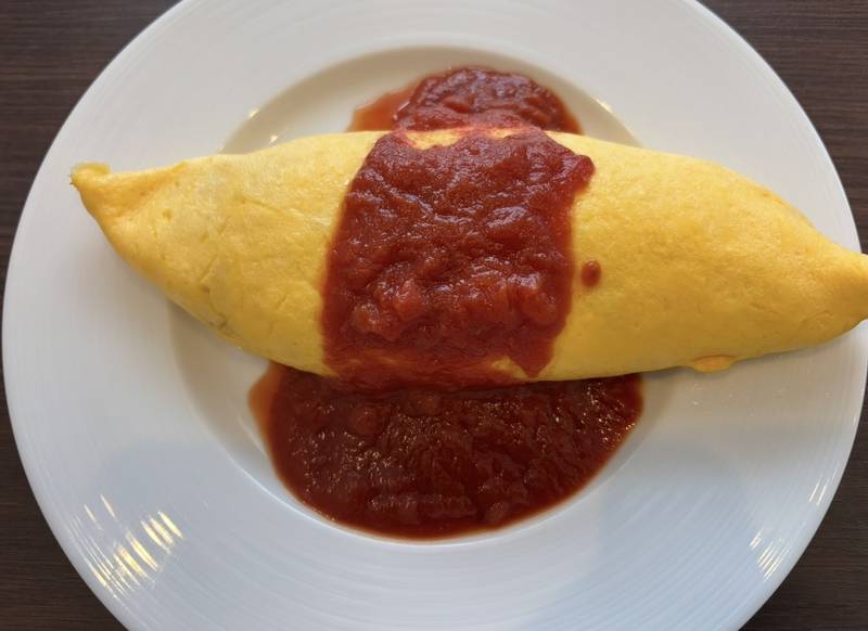 A fluffy yellow omelet rice dish generously topped with fresh tomato sauce.