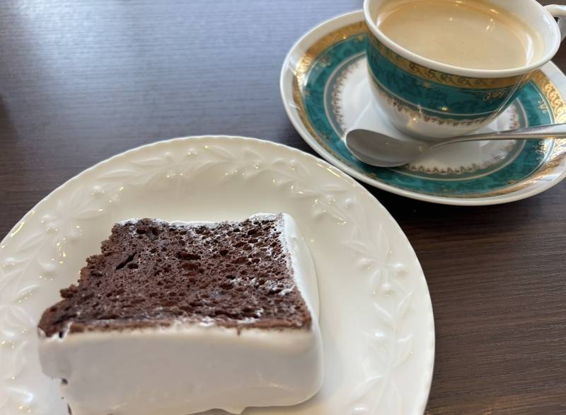 A fluffy cocoa chiffon cake with a generous border of fresh whipped cream, highlighting its moist texture. Served alongside a fragrant cup of hot coffee.