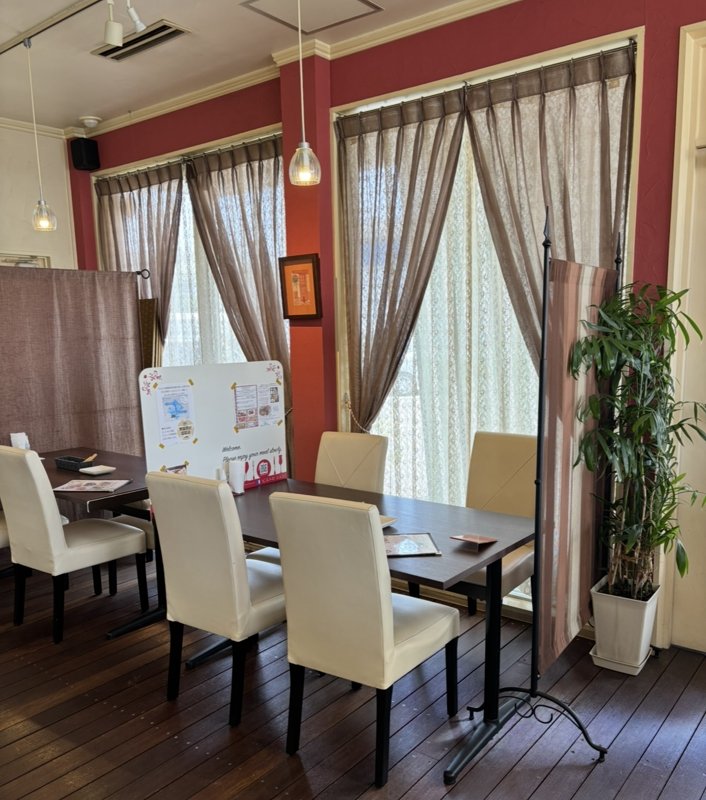 A cozy and elegant dining space with red walls, large windows, and lace curtains, creating a refined ambiance.