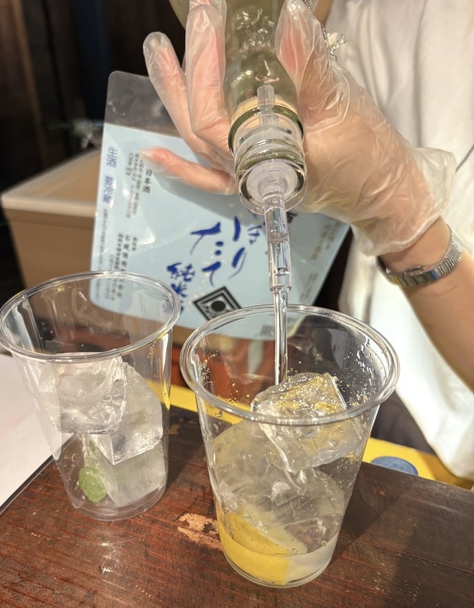 Preparation of “Junmai Squash” at an event, pouring freshly pressed junmai sake into a glass with ice and lemon syrup.