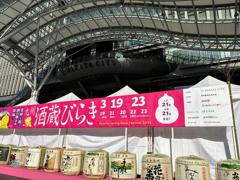 "Kyushu Sake Brewery Opening 2025" held in front of JR Hakata Station. Sake barrels from participating breweries lined up under the clear sky.