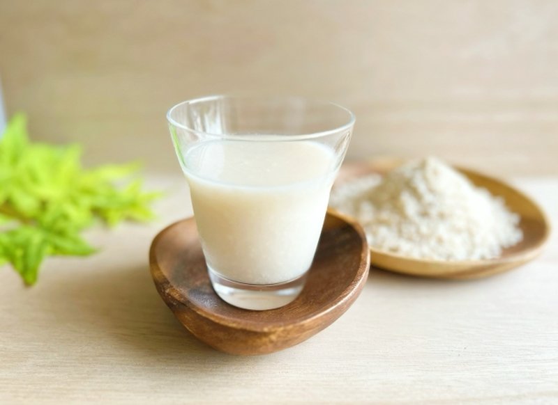English: A clear glass filled with koji amazake, placed beside a wooden plate with rice malt powder.