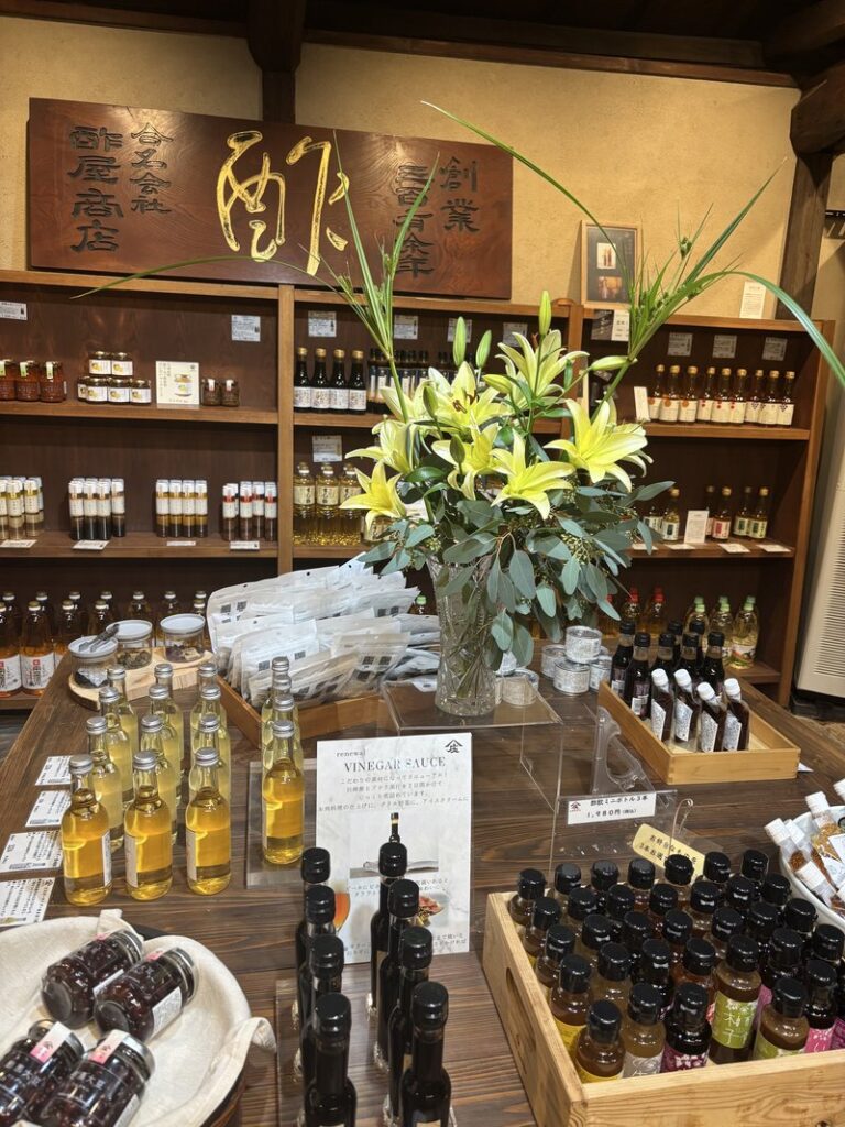 Shobunzu sales corner with fresh flowers and various vinegar products displayed on wooden shelves.
