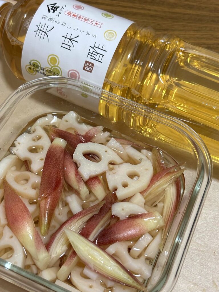Pickled lotus root and myoga in vinegar, stored in a clear container with vibrant colors.