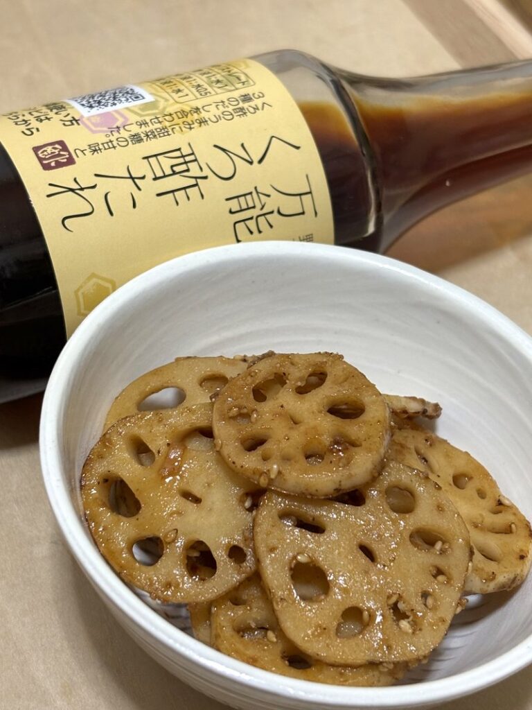 A bottle of versatile kurozu sauce with a dish of sweet and savory stir-fried lotus root served in a white bowl.