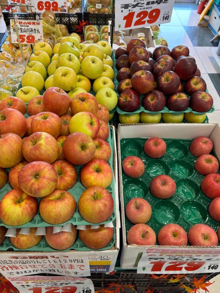 Four varieties of apples displayed at a supermarket fruit section, showing shades of red and green that evoke the feeling of autumn harvest.