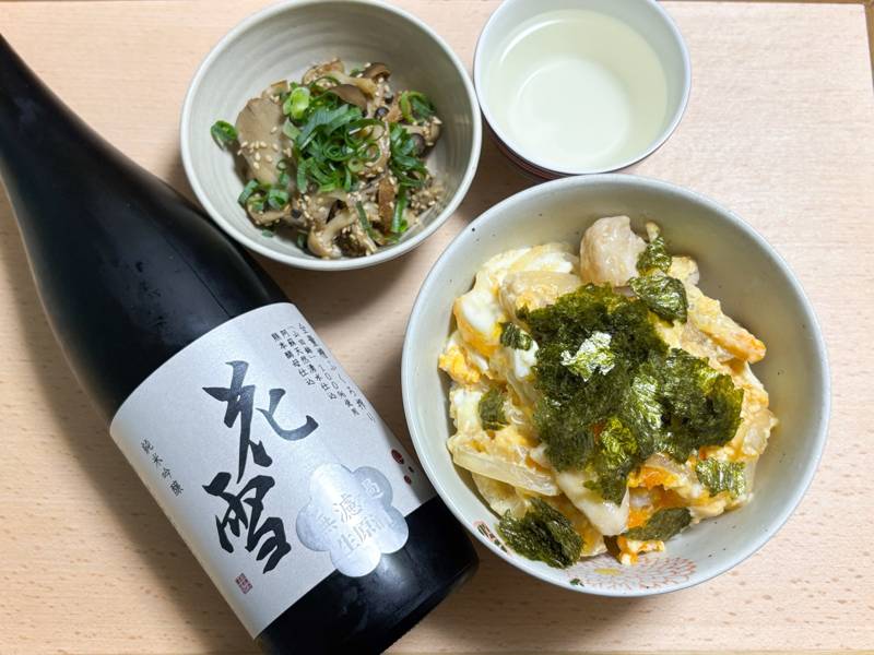 A bottle of Kawazu Brewery’s “Hanayuki” sake served with oyakodon, sesame-dressed mushrooms, and a chilled sake cup.