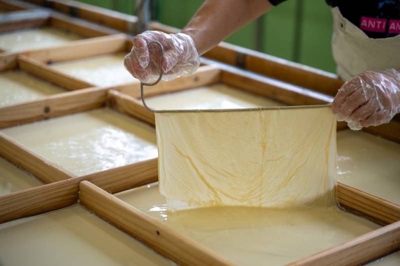 A craftsman carefully lifting a delicate sheet of yuba from the surface of heated soy milk.