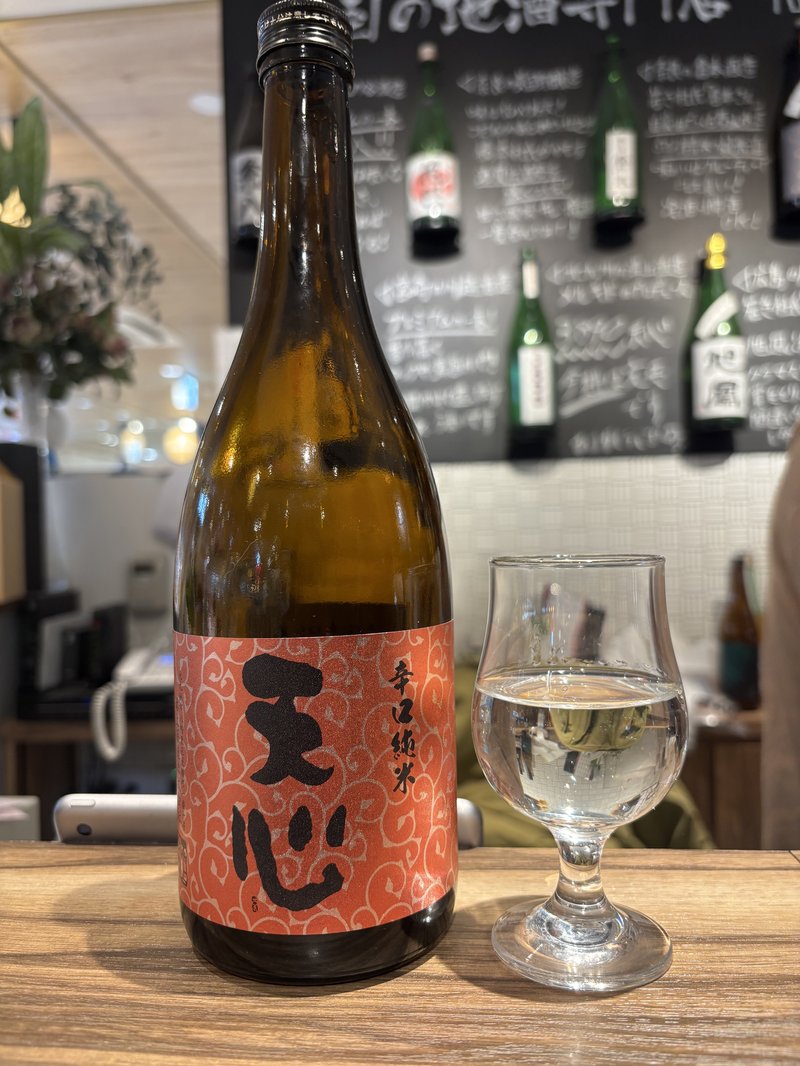 A bottle of Tenshin Junmai sake by Mizokami Shuzo, displayed on a counter with a glass of sake