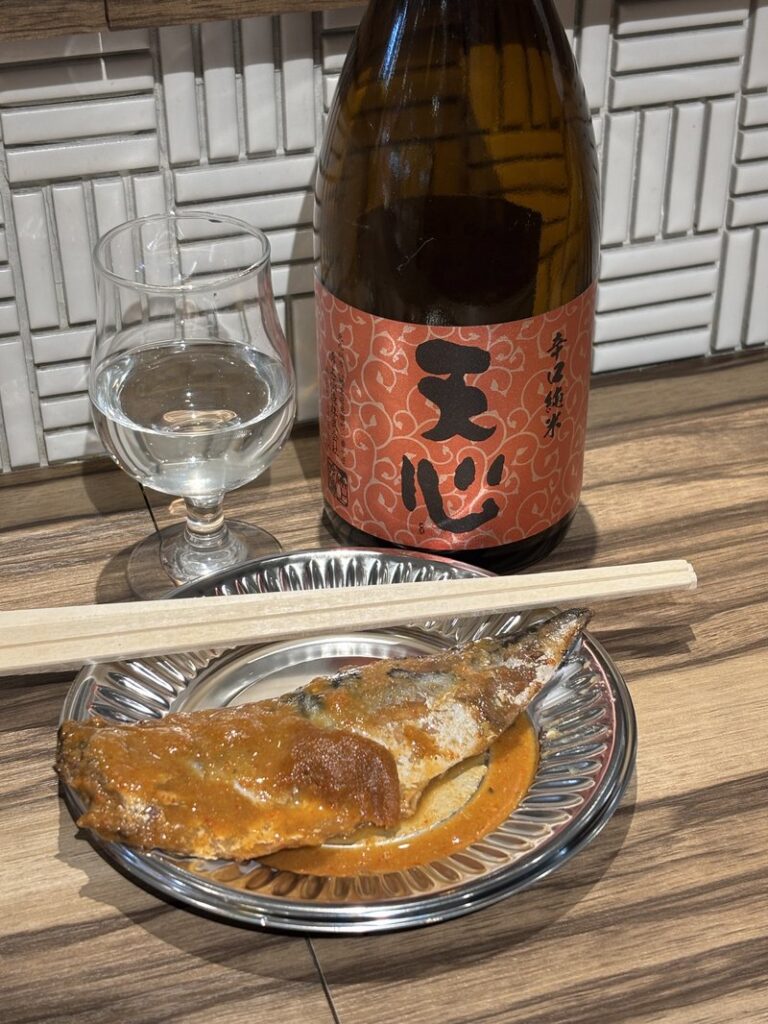 A plate of mackerel simmered in rice bran (saba nukadaki) paired with Tenshin sake by Mizokami Shuzo, served with a glass of sake