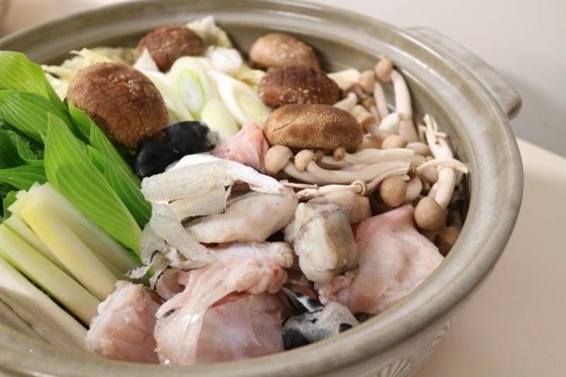 A fugu hot pot (fuguchiri) prepared with sliced pufferfish, vegetables, and mushrooms in a clay pot