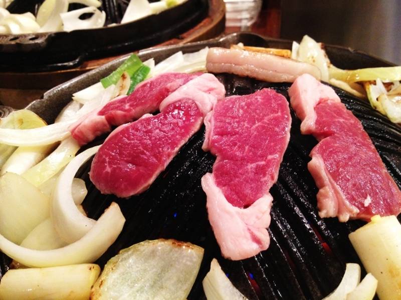 Slices of lamb and onions being grilled on a cast-iron jingisukan pan.