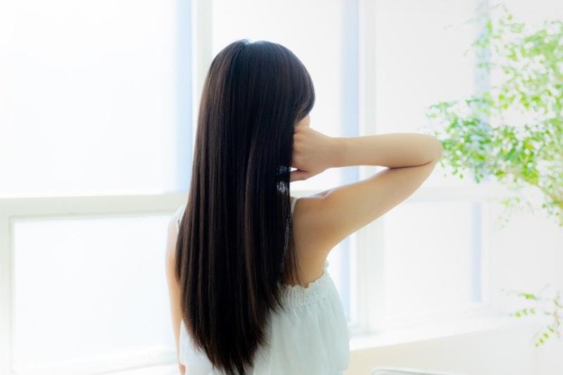 Image photo of a woman seen from behind, smoothing her long dark hair by a bright window
