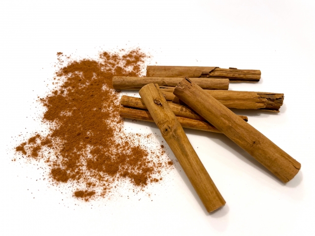 Image of several cinnamon sticks with ground cinnamon powder spread on a white background.