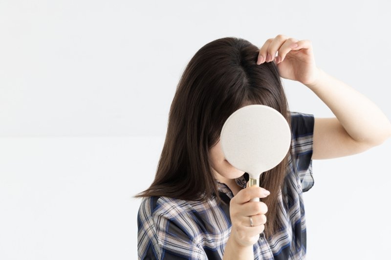 A woman holding a mirror and checking her scalp, representing hair and scalp concerns.