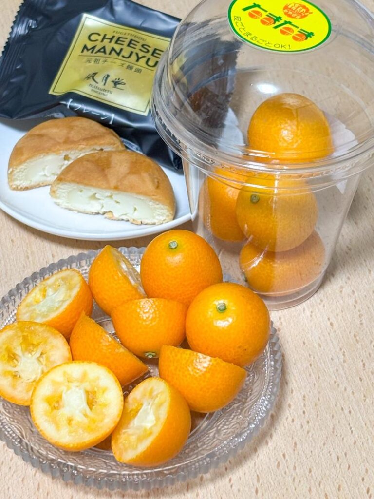 A table with whole and sliced kumquats alongside cheese manju pastries, one cut open to reveal the cream cheese filling.