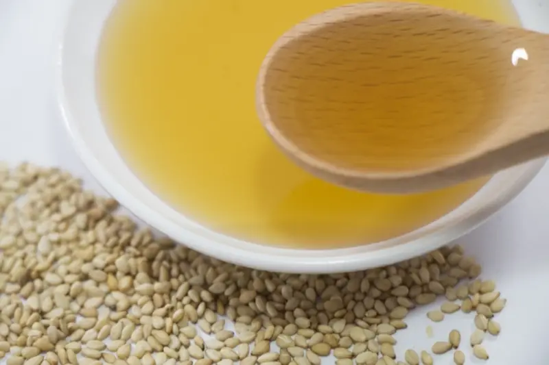 Golden sesame oil in a white bowl surrounded by white sesame seeds
