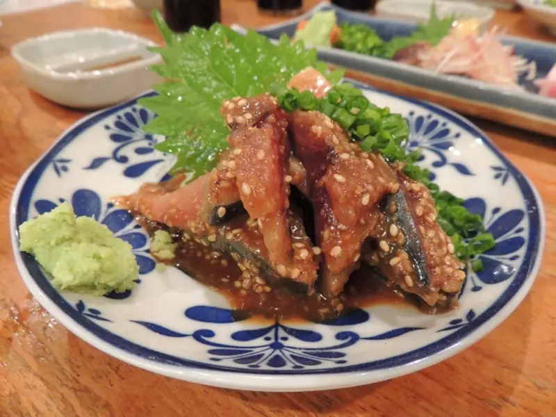 Hakata-style goma saba (sesame mackerel) served on a blue-and-white Arita-style plate, garnished with wasabi, green onions, and shiso leaf