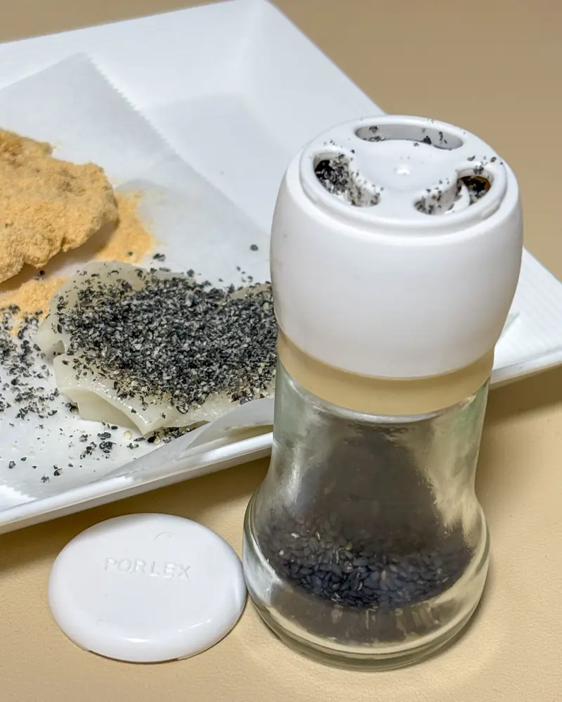 Porlex sesame mill with freshly ground black sesame seeds on a white plate