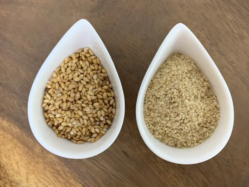 Two white teardrop-shaped dishes side by side: whole roasted sesame seeds on the left and ground sesame on the right