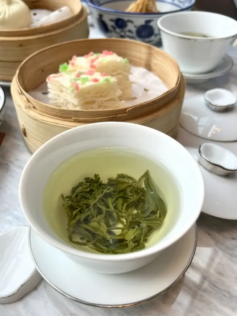 Chinese green tea poured into a teacup, with loose tea leaves scattered nearby.