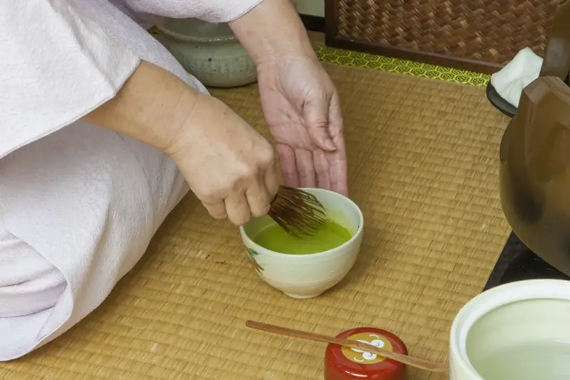 A tea ceremony scene with a tea bowl and chasen (bamboo whisk) placed on the tatami.